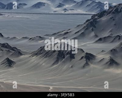Une route parfaitement droite traverse une étendue rugueuse de montagnes désertiques arides. La ligne humaine contraste avec le terrain sauvage et sec. Banque D'Images
