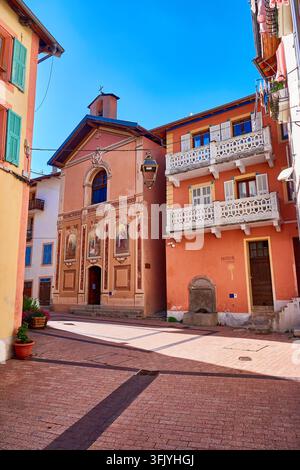 Place de village méditerranéen ensoleillée à Isola, France, avec façade d'église peinte et maisons colorées aux balcons Banque D'Images