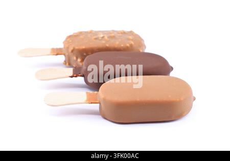 Trois glaces sur bâtonnets avec différents enrobages au chocolat : noir, au lait et à la praline. Fond blanc. Banque D'Images