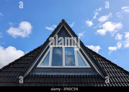 Section de toit triangulaire avec des tuiles sombres et une fenêtre moderne sous un ciel bleu vif Banque D'Images