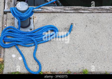 Corde bleu vif attachée autour d'un taquet métallique sur une jetée en béton, symbolisant la sécurité et la connexion Banque D'Images