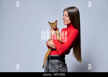 Femme souriante tenant un chat abyssin au profil isolé sur fond gris clair Banque D'Images