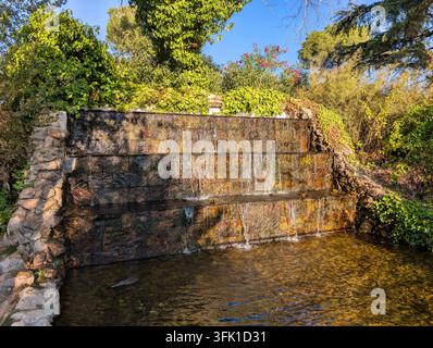 L'eau cascade le long d'une série de marches en pierre entourées de verdure dans un jardin. La scène montre un ciel clair et des éléments naturels. Banque D'Images