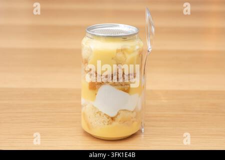 Dessert de gâteau mangue en couches avec une génoise au chocolat dans un récipient en boîte transparente et une cuillère sur une surface en bois. Banque D'Images
