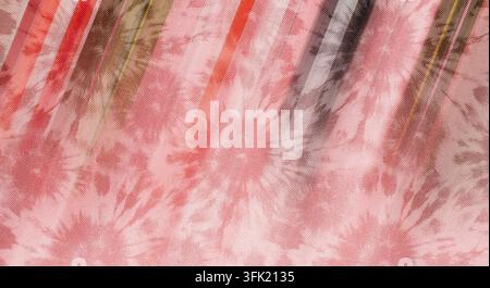 Un tissu tie-dye rose vif et rouge avec un design en éclat d'étoile et des accents de rayures diagonales, mettant en valeur une texture de matériau doux et plié. Banque D'Images