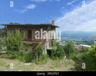 Maison inachevée avec des barres d'armature exposées et une végétation envahissante sur une colline dans un village rural près d'Olympie, en Grèce, offrant des vues panoramiques sur la di Banque D'Images
