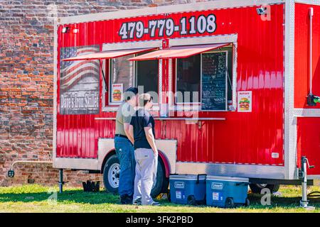 Arkansas, États-Unis, 07 AVR 2024 - Deux hommes discutent à côté d'un camion de restauration rouge vif nommé Daves Iron Skillet, garé sur l'herbe à côté d'une vieille brique Banque D'Images