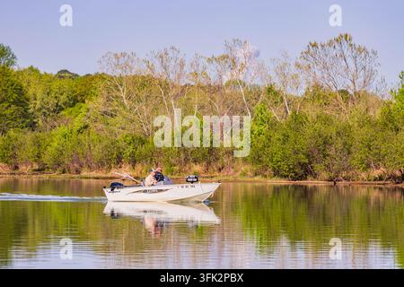 Arkansas, États-Unis, 08 AVR 2024 – Deux hommes pilotent un bateau à moteur blanc sur la surface miroir d'une rivière paisible bordée d'un vert luxuriant Banque D'Images