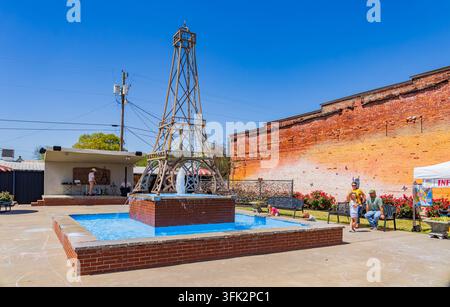 Arkansas, États-Unis, 07 avr. 2024 - Une réplique en bois de la Tour Eiffel s'élève derrière une fontaine en brique dans une place extérieure ensoleillée avec des gens Banque D'Images