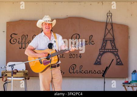Arkansas, États-Unis, 07 AVR 2024 - Un homme heureux portant un chapeau de cowboy joue une guitare acoustique en plein air devant un panneau décoratif pour Eiffel Banque D'Images