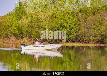 Arkansas, États-Unis, 08 AVR 2024 - Deux hommes sont assis dans un bateau à moteur blanc dérivant sur la surface miroir d'une rivière paisible bordée de végétation luxuriante Banque D'Images