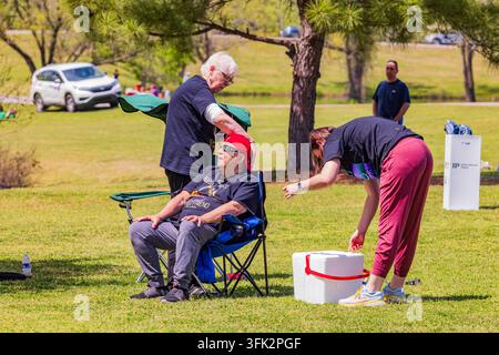Arkansas, États-Unis, 08 AVR 2024 – Deux aidants apportent une assistance à un homme âgé reposant sur une chaise pliante bleue dans un champ herbeux ensoleillé. Banque D'Images