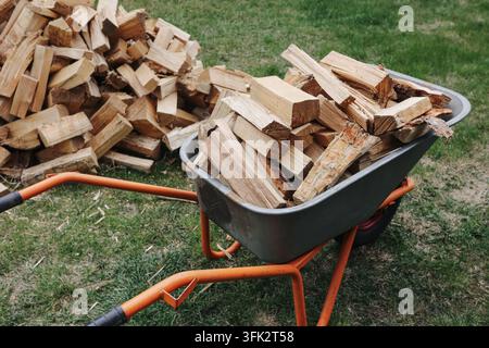 Brouette pleine de bois de chauffage coupé à l'extérieur. Fond en bois pour la préparation de combustible de chauffage, les fournitures de cheminée et l'énergie domestique saisonnière. Banque D'Images