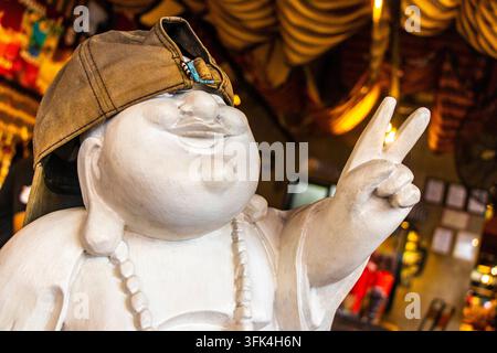 Figure de Bouddha assis blanc cool portant une casquette et montrant un signe de paix dans l'intérieur rustique du restaurant Naughty Nuris. Banque D'Images