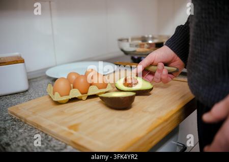 Personne coupant un avocat sur une planche en bois, préparant un repas sain avec des œufs frais Banque D'Images
