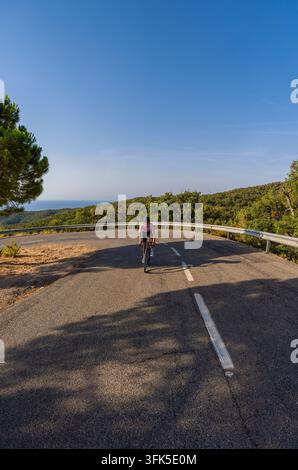 Un plan vertical en hauteur et en plein corps d'une jeune cycliste à vélo sur route hors de la selle le long d'une route montagneuse côtière sinueuse sur la Co Banque D'Images