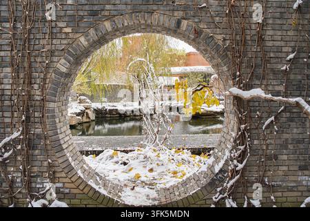 Scène enneigée et pièce d'eau encadrée par une porte de lune au Red Brick Art Museum à Pékin par une journée d'hiver Banque D'Images