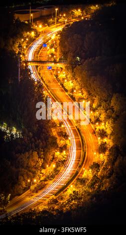 Prise verticale des traînées de lumière des voitures sur une route forestière sinueuse à Pékin la nuit Banque D'Images