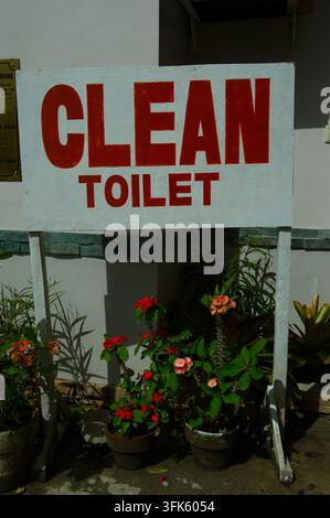 Une enseigne peinte à la main indiquant « Toilettes propres » affichée au-dessus de plantes en pot à l'extérieur d'un bâtiment aux Philippines. Banque D'Images