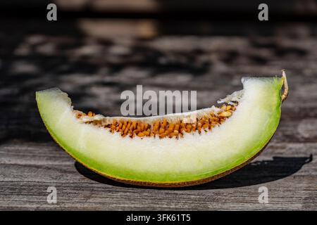 Tranche de melon vert frais avec des graines sur fond en bois, gros plan. Tranche juteuse de melon vert mûr ou cantaloup avec des graines orange posée sur un fond rustique Banque D'Images