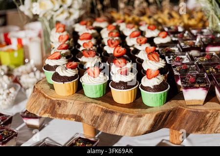 Cupcakes garnis de fraises avec un glaçage à la crème et des brownies au chocolat disposés sur des planches de service en bois pour un buffet de desserts lors d'un événement. Banque D'Images