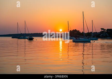 Yachts de voile ancrés dans une baie calme lors d'un coucher de soleil d'été coloré sur la mer. Soirée paisible, heure dorée, destination balnéaire et Banque D'Images