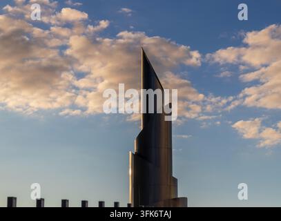Vue en contre-plongée d'une flèche de tour métallique moderne et torsadée contre un ciel nuageux au coucher du soleil. Banque D'Images
