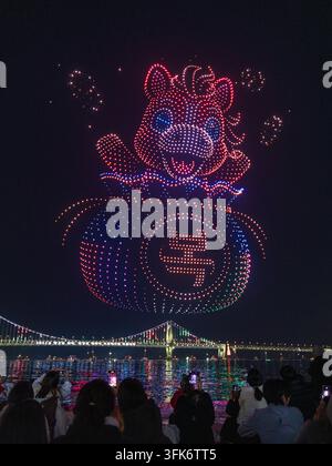 Busan, Busan, Corée du Sud - 14 février 2026 : Vue d'un spectacle de lumières de drones mettant en scène un personnage de dessin animé émergeant d'un sac au-dessus du Gwang illuminé Banque D'Images