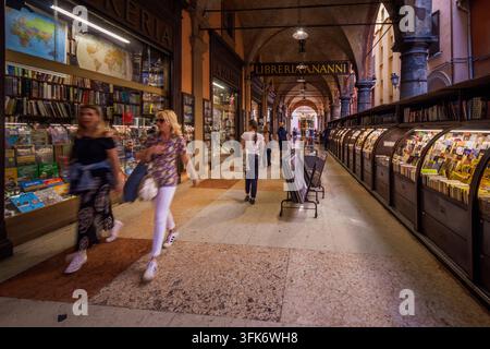 Bologne, Italie - 17 mai 2018 : Vue de la rue historique bordée de portiques à Bologne avec des gens passant devant une librairie traditionnelle et des vitrines extérieures Banque D'Images