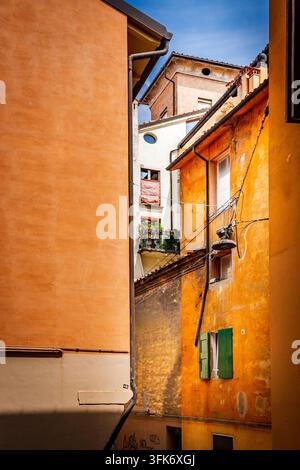 Bologne, Italie - 17 mai 2018 : Vue d'une ruelle étroite encadrée par des bâtiments historiques ocre et orange avec des volets verts et un petit balcon dans le c Banque D'Images