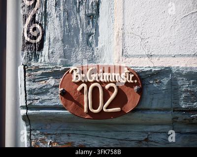 Plaque d'adresse ovale en terre cuite rustique portant l'inscription Br. Grimmstr. 102 fixée sur une porte en bois peinte en bleu usé à Steinau, Allemagne. Banque D'Images