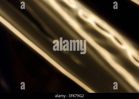 Photo abstraite en plein cadre de champagne chaud lumineux et de traînées de lumière dorées avec un mouvement ondulatoire fluide sur fond sombre. Concept de peinture lumineuse Banque D'Images