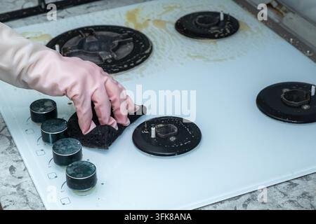 Une main dans un gant en caoutchouc rose essuie un plan de travail en verre avec une éponge. Banque D'Images