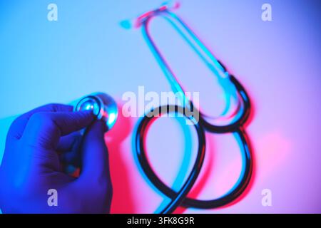 Main gantée d'un médecin tenant un stéthoscope, examinant avec des effets de lumière néon Banque D'Images
