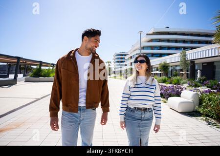 Jeune couple marchant et souriant dans un quartier moderne Banque D'Images