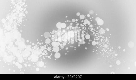 Un flux gracieux de cercles de bokeh blancs et de particules étincelantes balayant un fond texturé gris monochrome. Banque D'Images