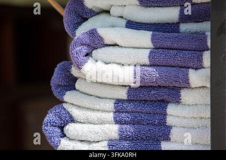 Pile de serviettes de bain bleues et blanches soigneusement pliées sur une étagère en bois au bord de la piscine d'un hôtel. Des serviettes propres et fraîches préparées pour les invités d'un resort de luxe Banque D'Images