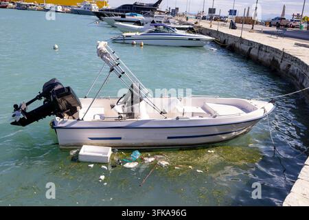 Petit bateau à moteur amarré dans le port de Zante en Grèce avec des bouteilles en plastique flottantes et des algues accumulées à côté de la coque tandis que plusieurs bateaux de loisirs Banque D'Images