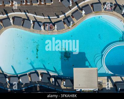 Vue aérienne depuis directement au-dessus d'une grande piscine de resort à Laganas Zakynthos Grèce montrant une eau turquoise, des transats, des parasols, un ponton et du boi Banque D'Images