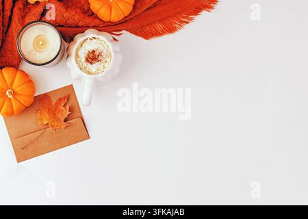 Latte au goût de citrouille avec mousse fouettée dans une tasse en forme de citrouille, bougie, petites citrouilles, écharpe tricotée orange et enveloppe kraft avec feuille d'érable sur fond blanc. Banque D'Images