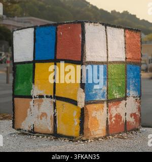 Grand bloc de béton peint comme un Rubik's Cube multicolore, utilisé comme barrière pour les véhicules sur un chemin cyclable. Banque D'Images