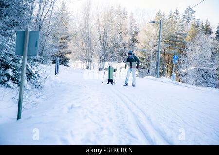 Un père aide son tout-petit à apprendre le ski de fond sur un sentier enneigé dans la région d'Helsinki, en Finlande, lors d'une sortie familiale active en hiver. Banque D'Images