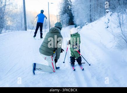 Un père aide son tout-petit à apprendre le ski de fond sur un sentier enneigé dans la région d'Helsinki, en Finlande, lors d'une sortie familiale active en hiver. Banque D'Images
