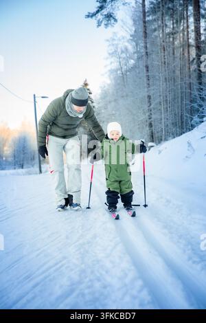Un père aide son tout-petit à apprendre le ski de fond sur un sentier enneigé dans la région d'Helsinki, en Finlande, lors d'une sortie familiale active en hiver. Banque D'Images