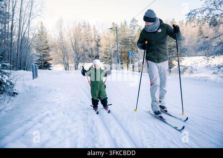Un père aide son tout-petit à apprendre le ski de fond sur un sentier enneigé dans la région d'Helsinki, en Finlande, lors d'une sortie familiale active en hiver. Banque D'Images