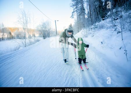 Un père aide son tout-petit à apprendre le ski de fond sur un sentier enneigé dans la région d'Helsinki, en Finlande, lors d'une sortie familiale active en hiver. Banque D'Images