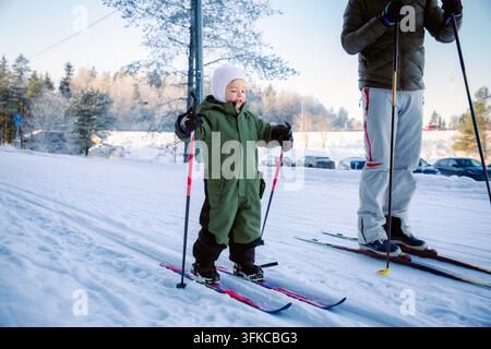 Un père aide son tout-petit à apprendre le ski de fond sur un sentier enneigé dans la région d'Helsinki, en Finlande, lors d'une sortie familiale active en hiver. Banque D'Images