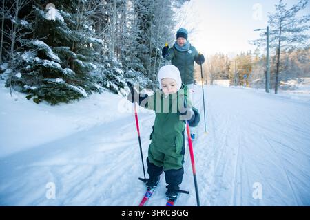 Un père aide son tout-petit à apprendre le ski de fond sur un sentier enneigé dans la région d'Helsinki, en Finlande, lors d'une sortie familiale active en hiver. Banque D'Images