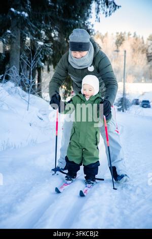 Un père aide son tout-petit à apprendre le ski de fond sur un sentier enneigé dans la région d'Helsinki, en Finlande, lors d'une sortie familiale active en hiver. Banque D'Images