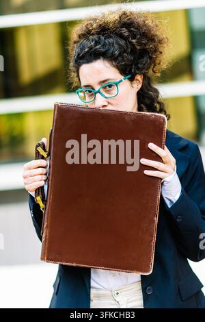 Femme d'affaires se cachant derrière une mallette et regardant par-dessus ses lunettes Banque D'Images